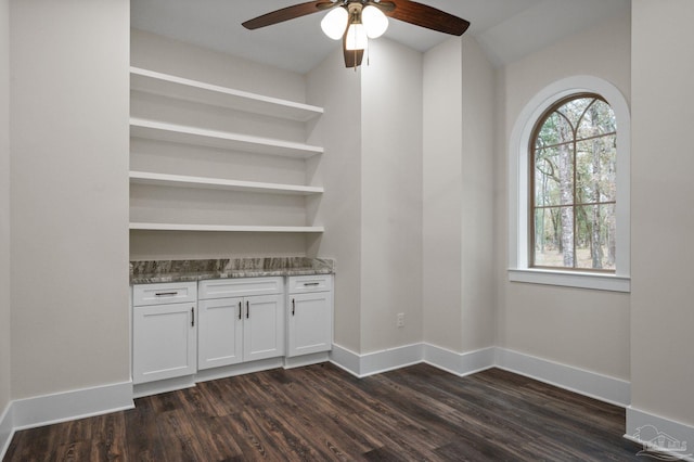 unfurnished room with dark wood finished floors, a ceiling fan, and baseboards