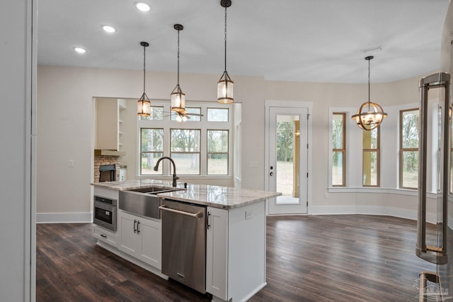 kitchen featuring a kitchen island with sink, a sink, dark wood-style floors, stainless steel appliances, and light stone countertops