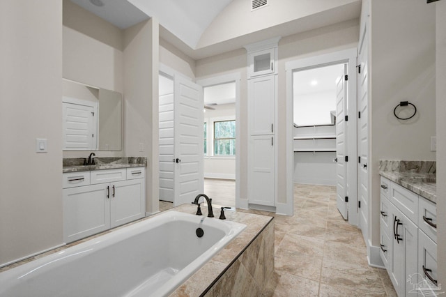 bathroom featuring tiled bath, lofted ceiling, two vanities, a closet, and a sink