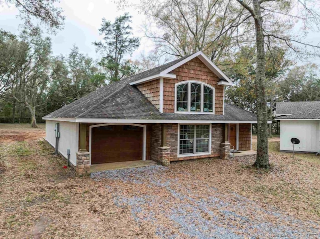 view of front of house with stone siding, roof with shingles, gravel driveway, and an attached garage