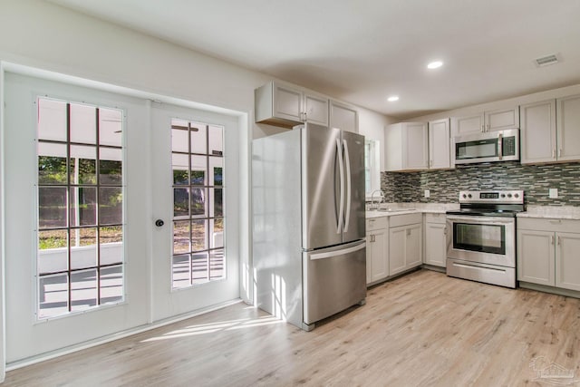 kitchen featuring decorative backsplash, appliances with stainless steel finishes, light wood-type flooring, sink, and gray cabinets