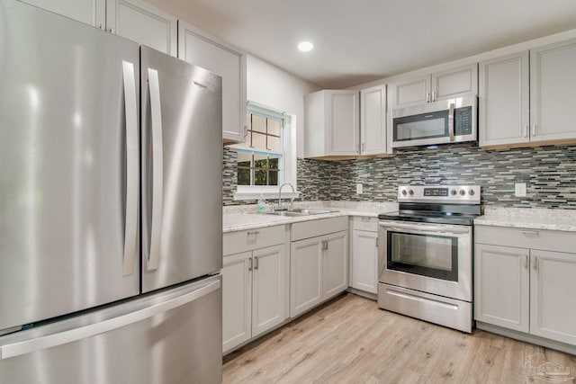 kitchen featuring backsplash, sink, light hardwood / wood-style flooring, appliances with stainless steel finishes, and light stone counters