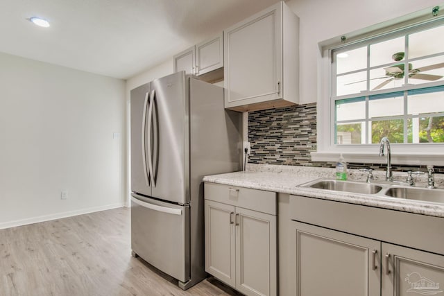 kitchen featuring backsplash, stainless steel refrigerator, sink, and light wood-type flooring