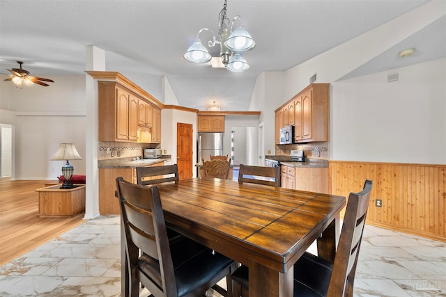 dining area featuring lofted ceiling, wooden walls, ceiling fan with notable chandelier, and light wood-type flooring