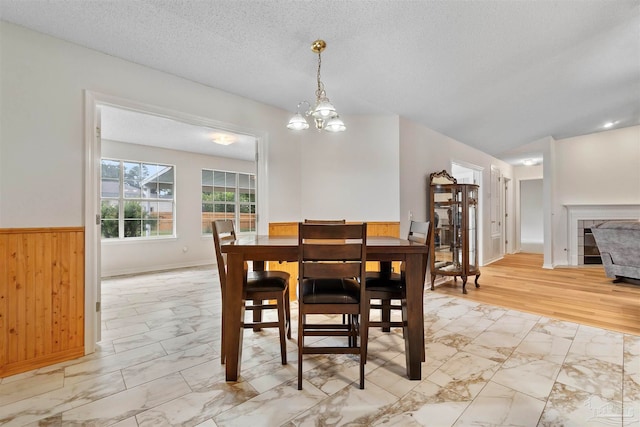 dining area with light wood-type flooring, wooden walls, a textured ceiling, and an inviting chandelier