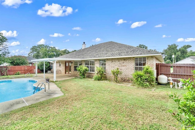 rear view of property with a yard, a patio area, and a fenced in pool