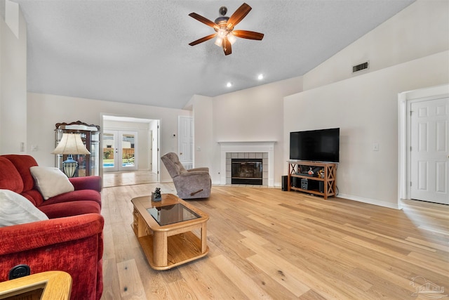 living room featuring wood-type flooring, a fireplace, a textured ceiling, ceiling fan, and high vaulted ceiling