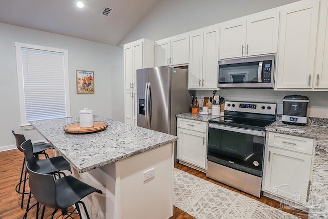 kitchen with light stone counters, a center island, white cabinets, appliances with stainless steel finishes, and a kitchen breakfast bar