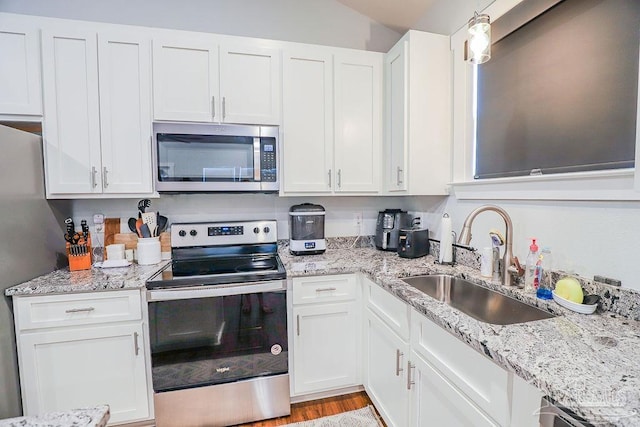 kitchen with light stone counters, stainless steel appliances, light hardwood / wood-style floors, white cabinetry, and sink