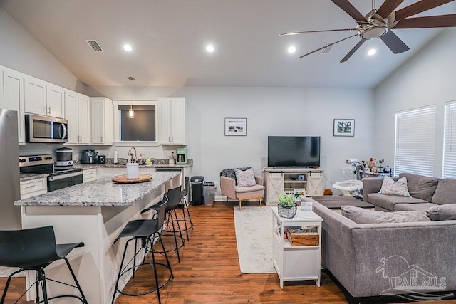 kitchen featuring a breakfast bar area, vaulted ceiling, light stone counters, and appliances with stainless steel finishes