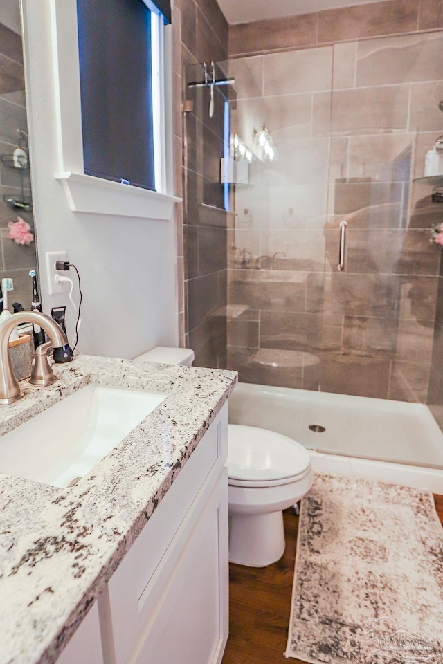 bathroom featuring toilet, vanity, hardwood / wood-style floors, and tiled shower