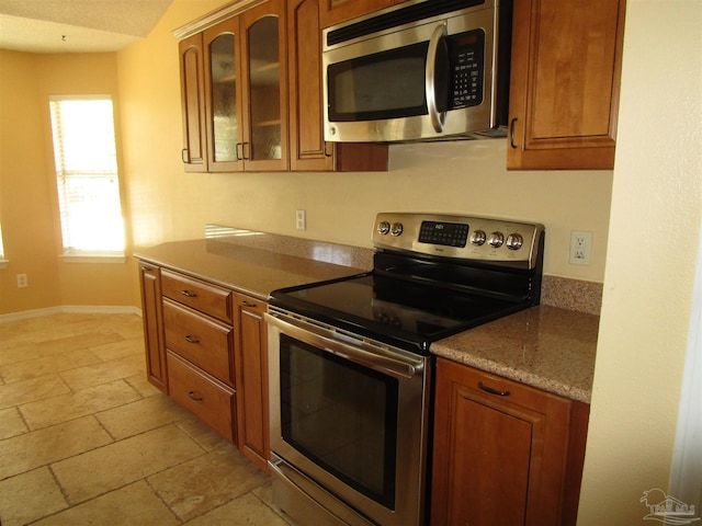 kitchen with stone tile flooring, brown cabinetry, and appliances with stainless steel finishes