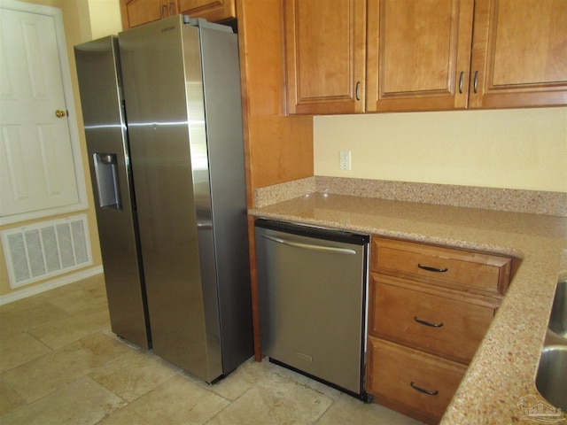 kitchen with brown cabinetry, stone finish floor, visible vents, and stainless steel appliances