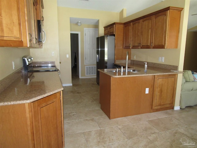 kitchen featuring visible vents, a sink, a peninsula, brown cabinetry, and range