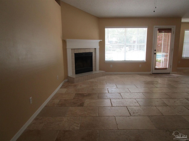unfurnished living room featuring a fireplace, baseboards, and stone tile flooring