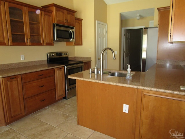 kitchen featuring a sink, glass insert cabinets, brown cabinetry, and appliances with stainless steel finishes