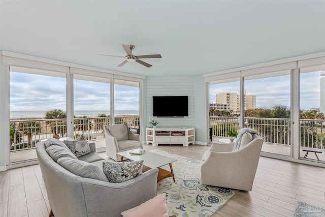 living room with light wood-type flooring, ceiling fan, a wall of windows, and a water view