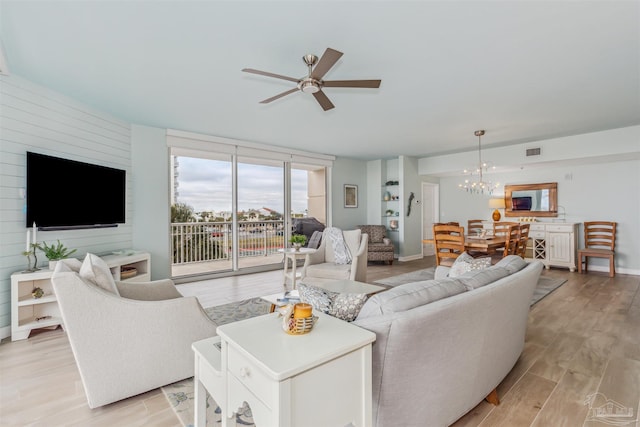 living room featuring ceiling fan with notable chandelier and light hardwood / wood-style flooring