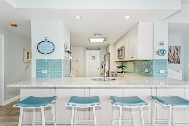 kitchen with white cabinets, decorative backsplash, sink, kitchen peninsula, and a breakfast bar