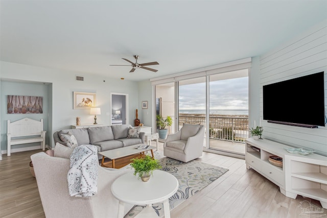 living room featuring wooden walls, ceiling fan, light hardwood / wood-style floors, and expansive windows