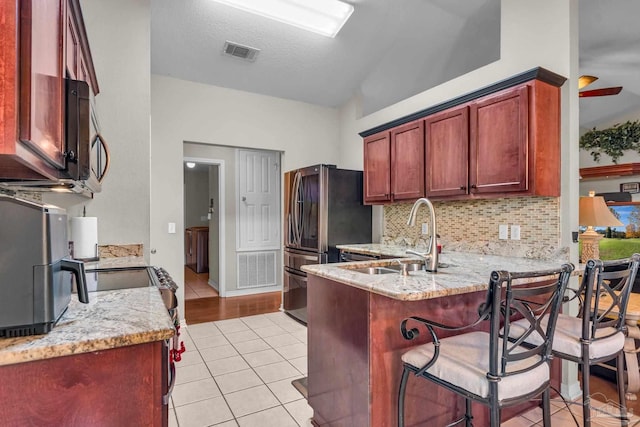 kitchen with sink, stainless steel fridge, light tile patterned floors, light stone counters, and kitchen peninsula