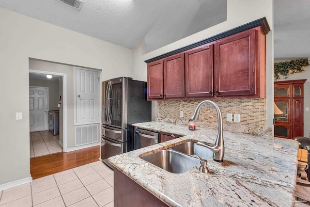 kitchen with sink, light stone countertops, light tile patterned floors, appliances with stainless steel finishes, and tasteful backsplash