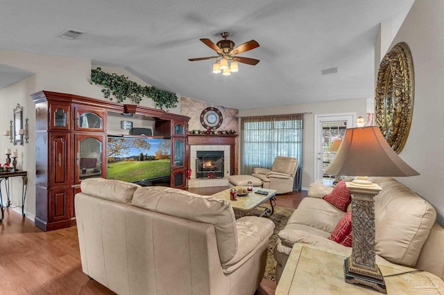 living room with a textured ceiling, vaulted ceiling, ceiling fan, hardwood / wood-style floors, and a tiled fireplace