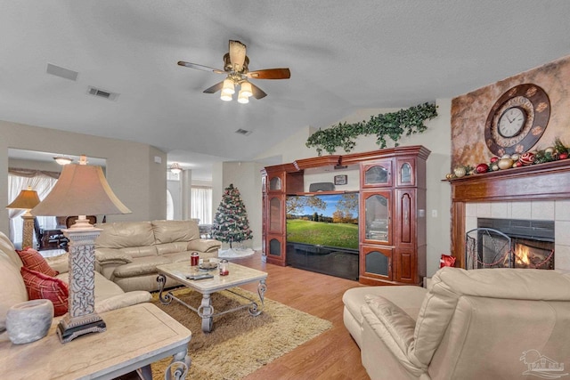 living room featuring a tile fireplace, vaulted ceiling, ceiling fan, light wood-type flooring, and a textured ceiling