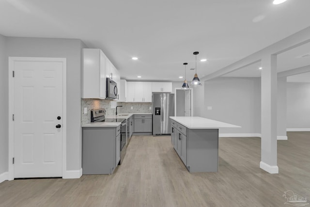 kitchen featuring a center island, appliances with stainless steel finishes, gray cabinets, hanging light fixtures, and light hardwood / wood-style flooring