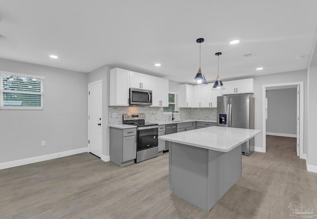 kitchen with stainless steel appliances, white cabinetry, decorative light fixtures, light hardwood / wood-style flooring, and a center island