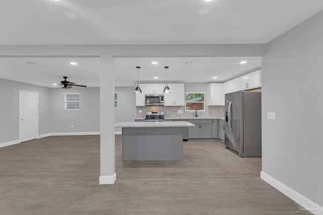 kitchen with stainless steel appliances, white cabinetry, decorative light fixtures, light hardwood / wood-style flooring, and a kitchen island