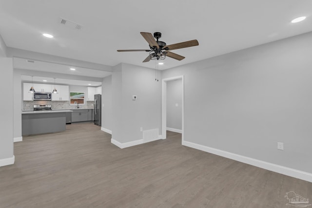 unfurnished living room with sink, ceiling fan, and light hardwood / wood-style flooring