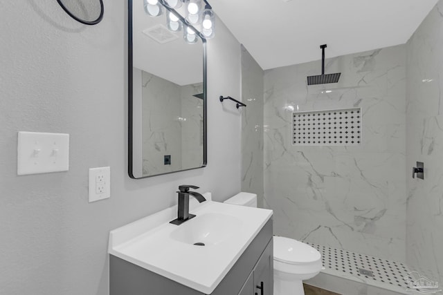 bathroom with tiled shower, vanity, and toilet