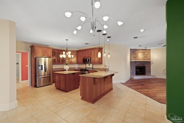 kitchen featuring an inviting chandelier, appliances with stainless steel finishes, light hardwood / wood-style floors, kitchen peninsula, and a brick fireplace