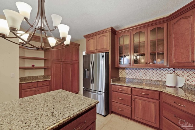 2715 Masters Blvd, Navarre, FL 32566 - kitchen with stainless steel fridge with ice dispenser, a chandelier, light stone counters, glass insert cabinets, and decorative backsplash
