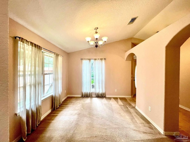 carpeted empty room with a notable chandelier, a textured ceiling, and vaulted ceiling