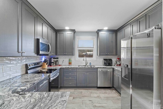 kitchen featuring light stone countertops, appliances with stainless steel finishes, sink, and backsplash