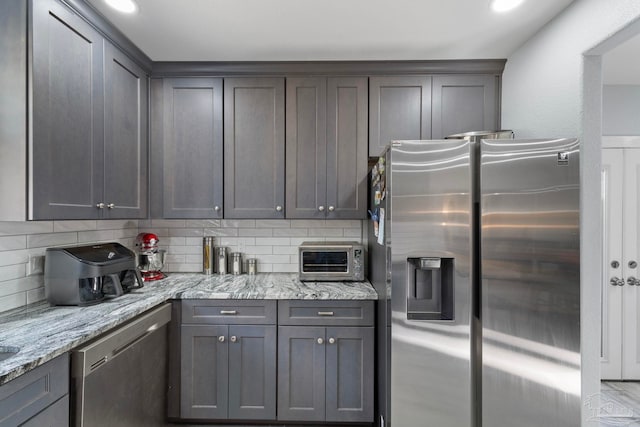 kitchen featuring appliances with stainless steel finishes, backsplash, and light stone counters