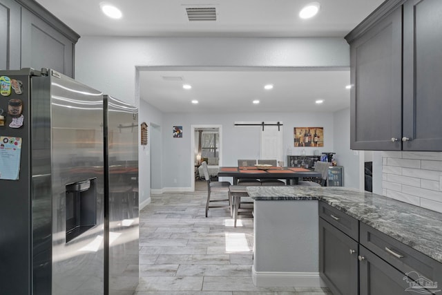 kitchen featuring gray cabinets, a barn door, dark stone countertops, and stainless steel fridge