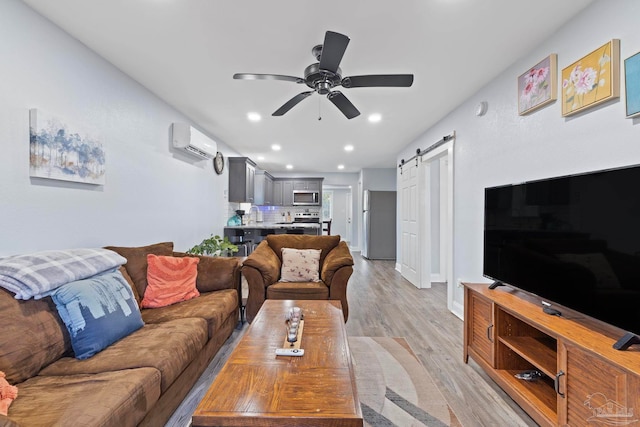 living room featuring sink, a wall mounted air conditioner, light wood-type flooring, ceiling fan, and a barn door