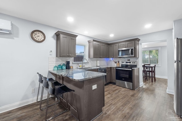 kitchen with decorative backsplash, light stone countertops, kitchen peninsula, and appliances with stainless steel finishes