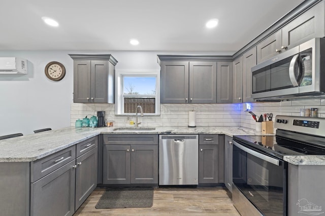 kitchen with appliances with stainless steel finishes, sink, light stone counters, kitchen peninsula, and light hardwood / wood-style flooring