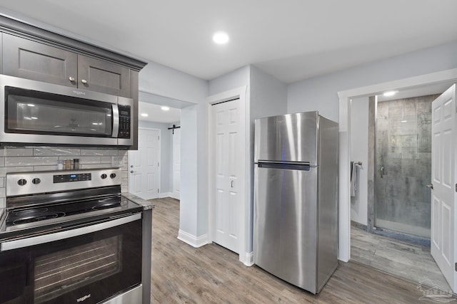 kitchen featuring light hardwood / wood-style flooring, dark brown cabinets, stainless steel appliances, tasteful backsplash, and a barn door