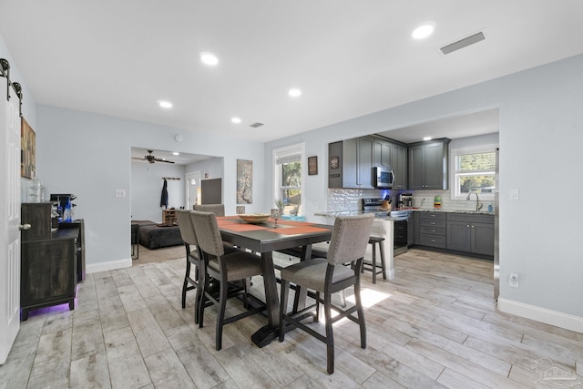 dining room with sink, light hardwood / wood-style flooring, a barn door, and ceiling fan