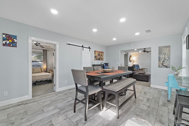 dining area with ceiling fan, a barn door, and light wood-type flooring