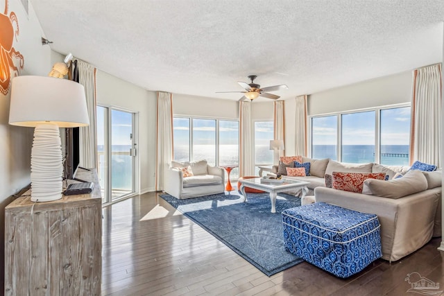 living room with a textured ceiling, a water view, wood finished floors, and ceiling fan