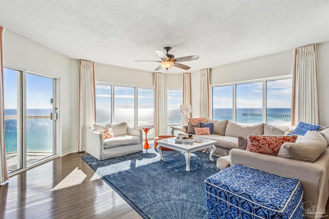living room featuring ceiling fan, wood-type flooring, a textured ceiling, baseboards, and a water view