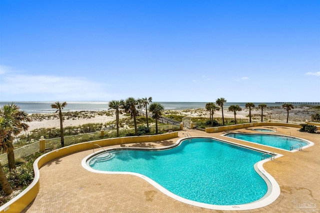 pool featuring a patio, a water view, and a hot tub