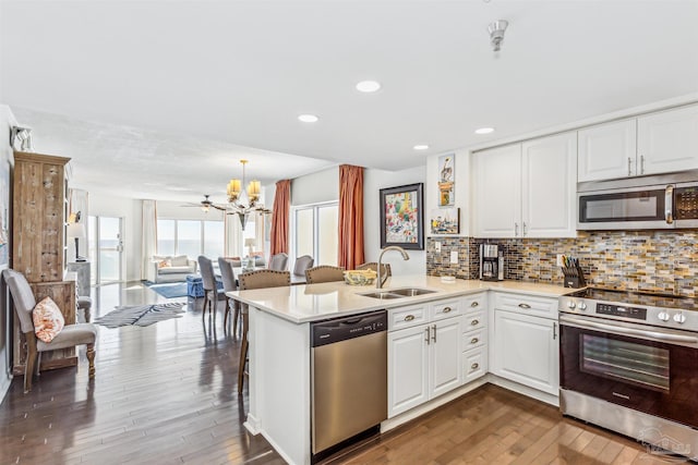 kitchen with a notable chandelier, a sink, dark wood finished floors, stainless steel appliances, and a peninsula