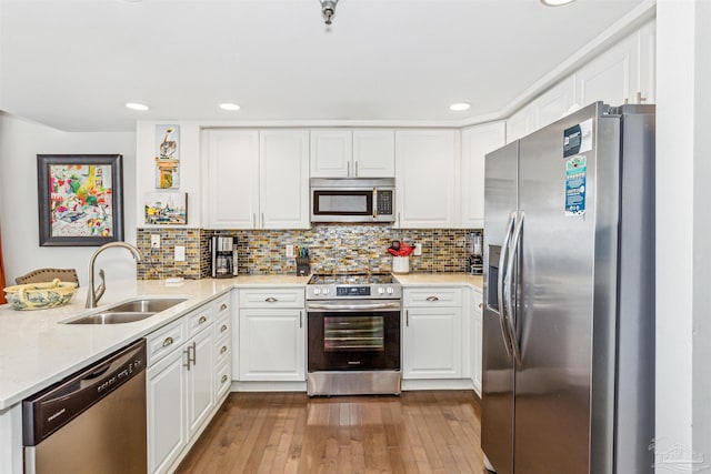 kitchen with wood-type flooring, recessed lighting, white cabinetry, a sink, and appliances with stainless steel finishes
